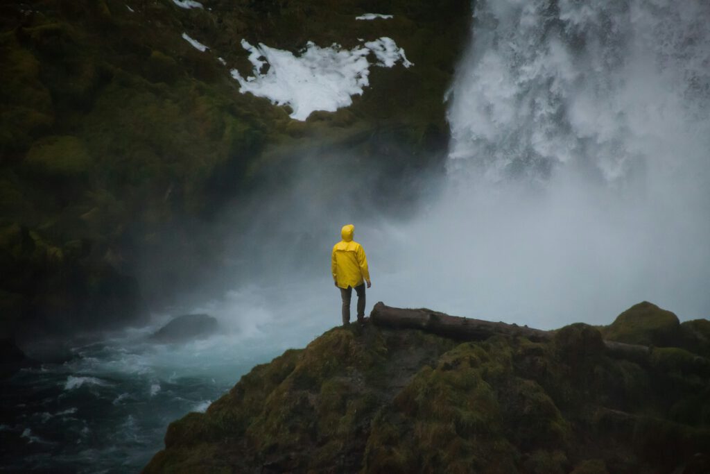 A person in a yellow rain coat standing alone near a powerful waterfall in a misty forest. | Therapy in Portland, Oregon helping overwhelmed adults feel more grounded and present in their lives